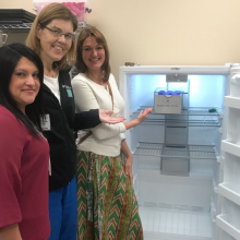 Three women standing next to an open upright freezer