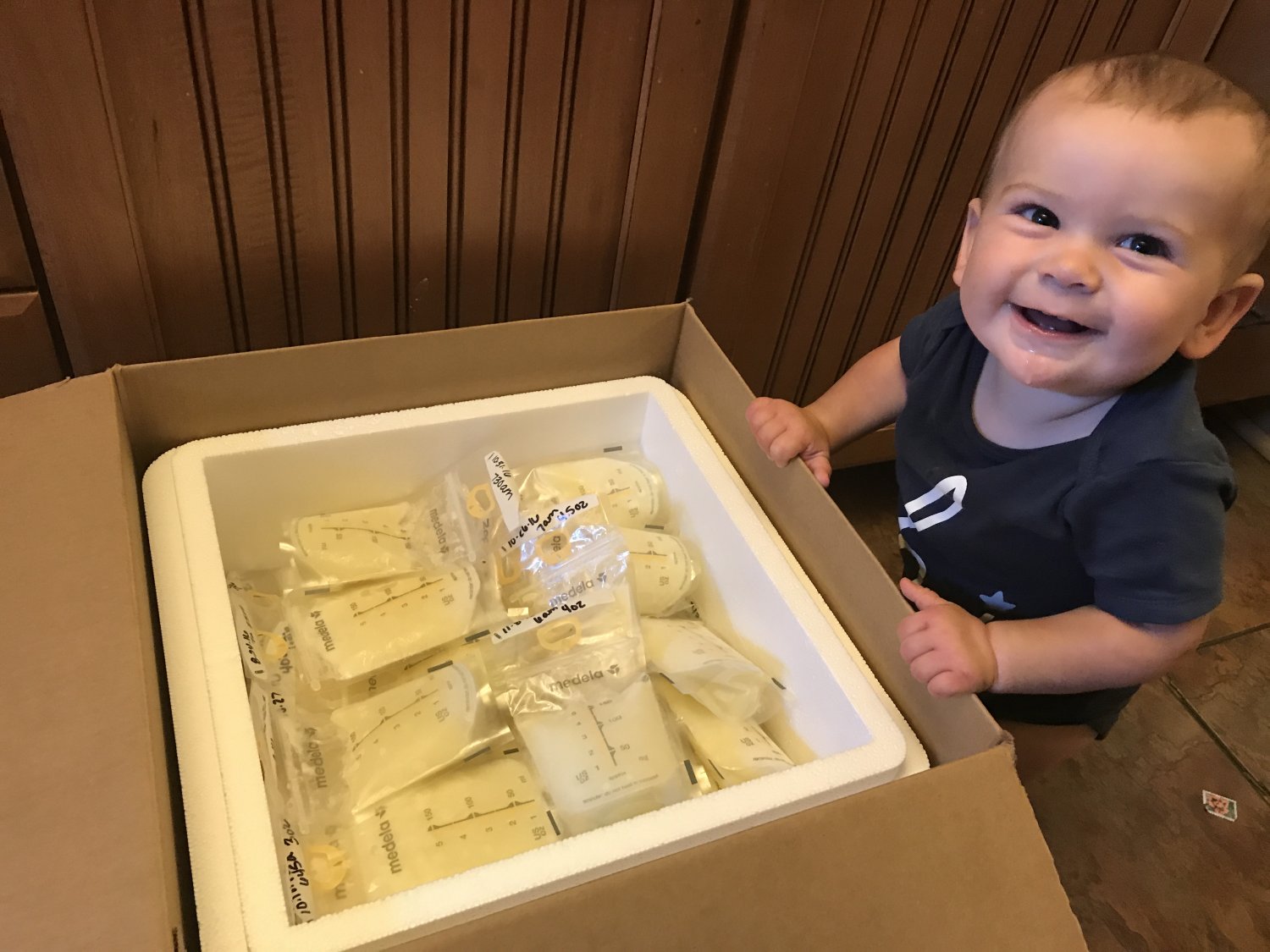 Baby sitting next to cooler of frozen breastmilk